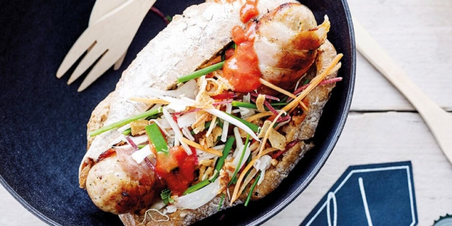 Hotdog met worst en spek, chipotlesaus, rauwkost en gefrituurde ui